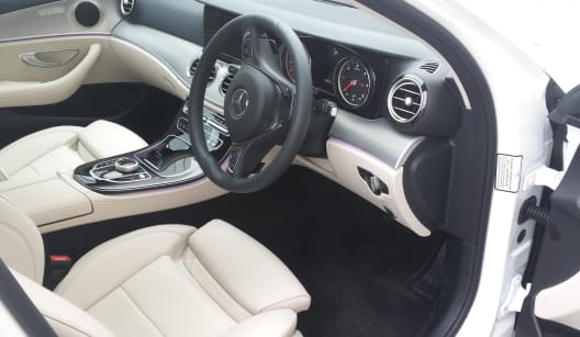 The drivers side interior of a white two seater Mercedes E Class luxury saloon car