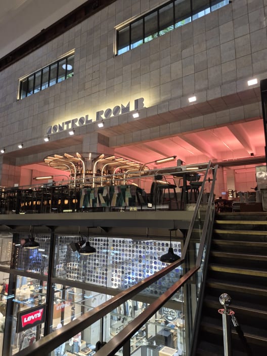 An internal view of the Control Room B bar inside Battersea Power Station, featuring a retro bar setup with pink ambient lighting above a retail level.