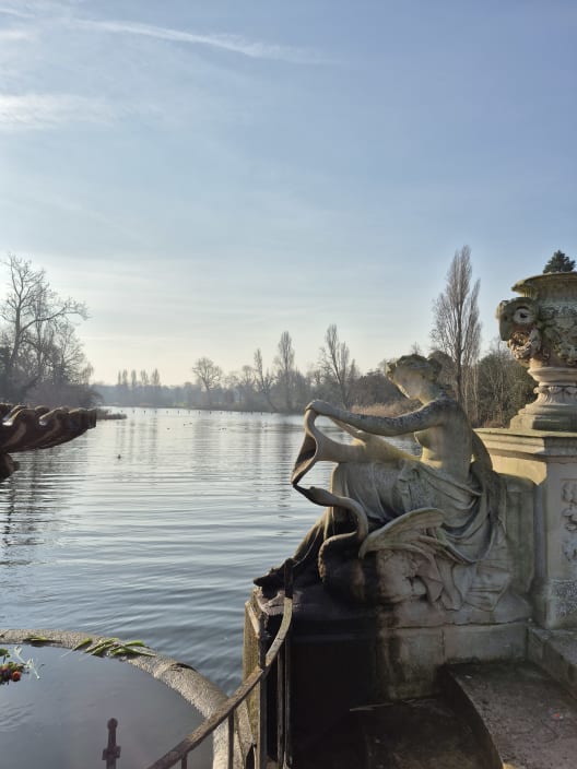 A classical stone statue of a woman and a swan beside the water at the Italian Gardens in Kensington Gardens, London.