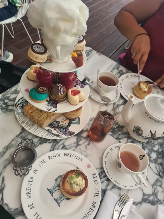 A marble table set for an Alice in Wonderland themed afternoon tea, featuring a tiered stand of pastries, whimsical teacups, and a large cloud of cotton candy.