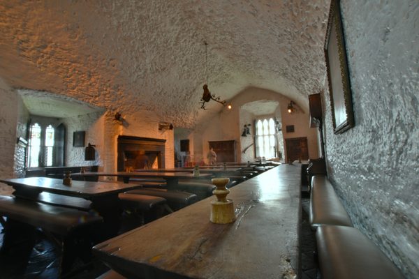 The Main Guard inside Bunratty Castle, a long room under a low white barrel vault, with bare timber tables, a fireplace and exhibition panels along the walls