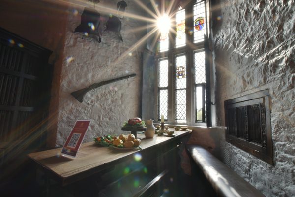 Sunlight bursting through the stained-glass window onto a table laid with fruit, vegetables and cups inside Bunratty Castle