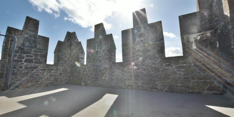 The crenellated battlements at the top of Bunratty Castle, with the sun breaking through the stone