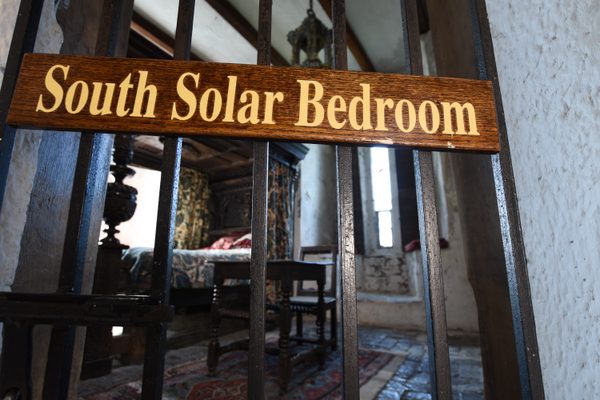 The carved South Solar Bedroom sign on the gate, with the bed and drapery of the room beyond, inside Bunratty Castle