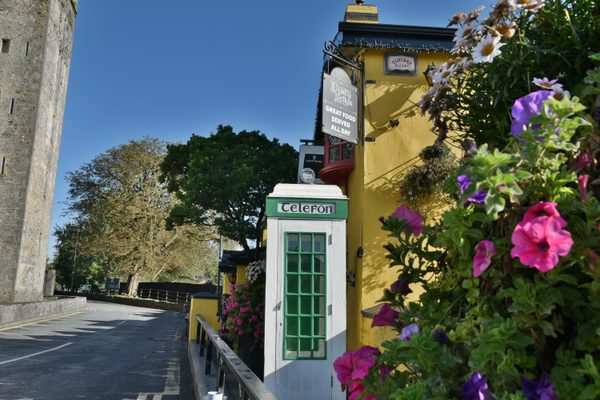 The green telephone box in Bunratty village, with hanging baskets of flowers and a yellow-walled building beside it