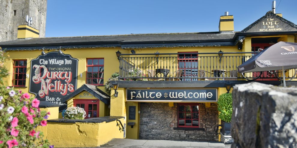 The yellow frontage of Durty Nelly's in Bunratty, with flowers and a Fáilte and Welcome sign