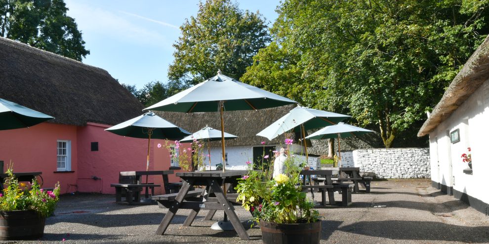The courtyard seating and tea room at Bunratty Folk Park, with parasols and a thatched cottage behind