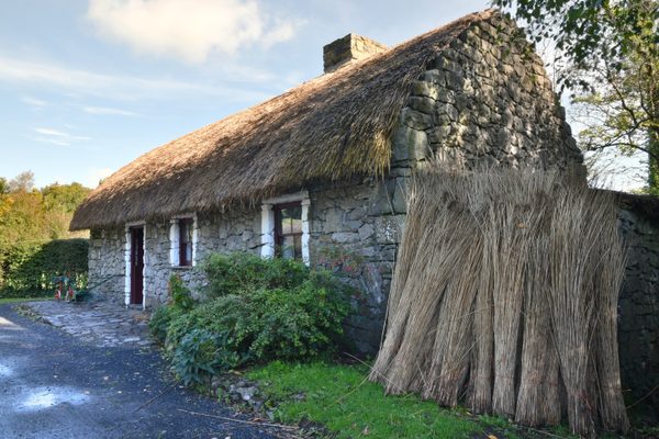 A stone thatched cottage at Bunratty Folk Park, with a stack of straw leaning against its gable