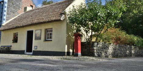 A cottage with a red door at Bunratty Folk Park, with a figure in period dress beside it