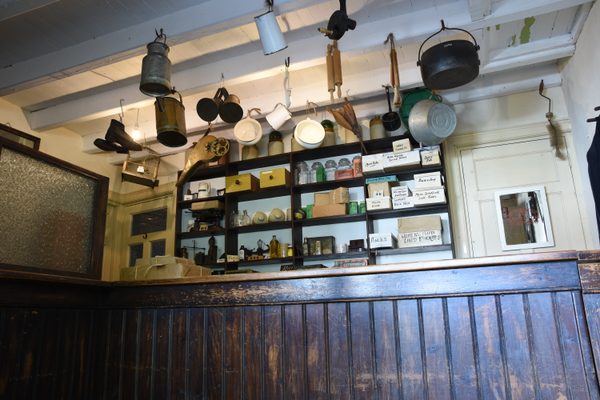 The interior of the post office at Bunratty Folk Park, with its green-painted door and window, a red post box set into the wall and a red postman's handcart outside, with the yellow McInerney & Sons shop across the street